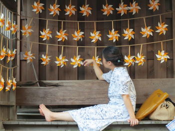 Side view of woman playing with pinwheel decoration sitting on bench