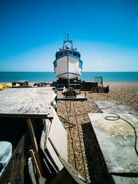 Blue and white boat on shingle beach with sea behind and blue skies 