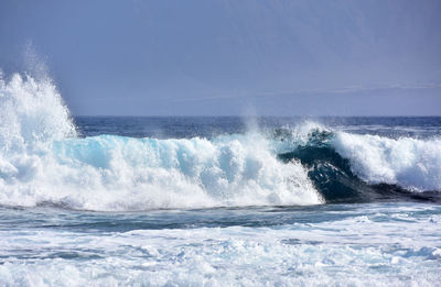 Waves splashing on sea against clear blue sky