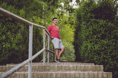 Portrait of smiling young man standing by railing against trees