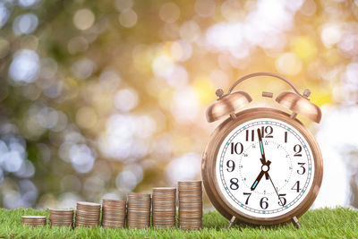 Close-up of alarm clock with coins on grassy field