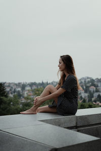 Side view of young woman sitting against sky