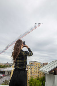 Rear view of woman photographing airplane flying in sky