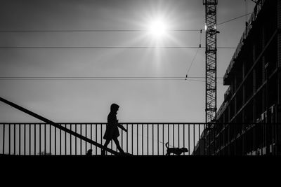 Silhouette man walking on footbridge against sky