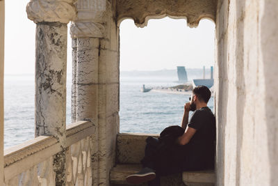 Side view of woman sitting by sea against sky