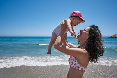 Woman with daughter on beach against sky