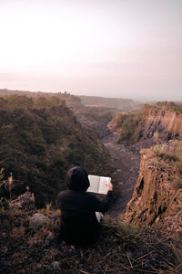 Rear view of man sitting on landscape against sky