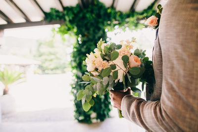 Midsection of bridegroom holding flower bouquet at home