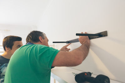 Father with son fixing rack on white wall