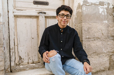 Young transgender man posing sitting on the front steps of a house.