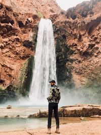 Full length of man standing on rock against waterfall