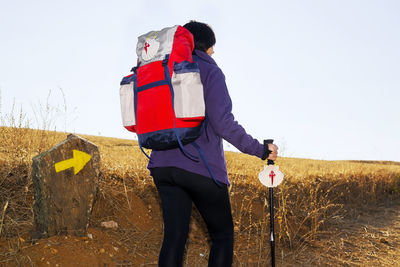 Rear view of female hiker walking on field against clear sky
