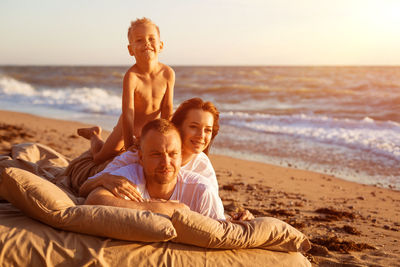 Cheerful family lying on mattress at beach during sunset