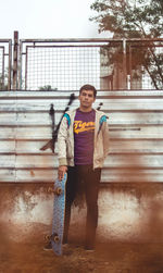 Man with skateboard standing against corrugated iron