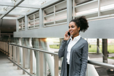 Businesswoman using phone while standing by railing