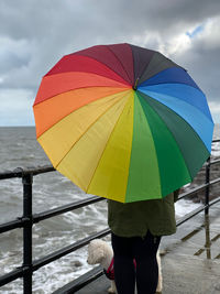 Midsection of woman standing by multi colored umbrella against sky during rainy season