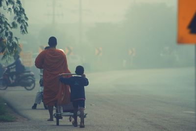Rear view of monk and boy walking on road during foggy weather