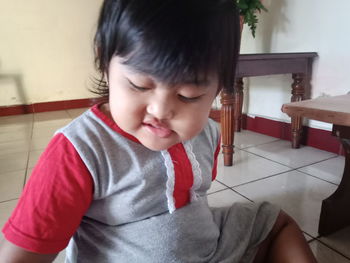 Cute boy looking away while sitting on floor at home