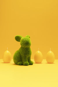 Green easter bunny, rabbit with three yellow candles of eggs shape on matching monochrome orange