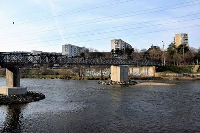 Bridge over river by buildings against sky