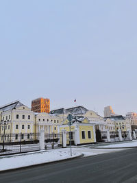 Road by buildings against clear sky during winter