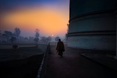 Rear view of monk by temple during sunset