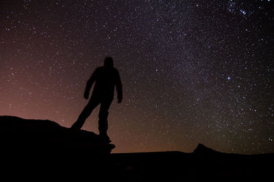 Silhouette man standing on cliff against sky at night