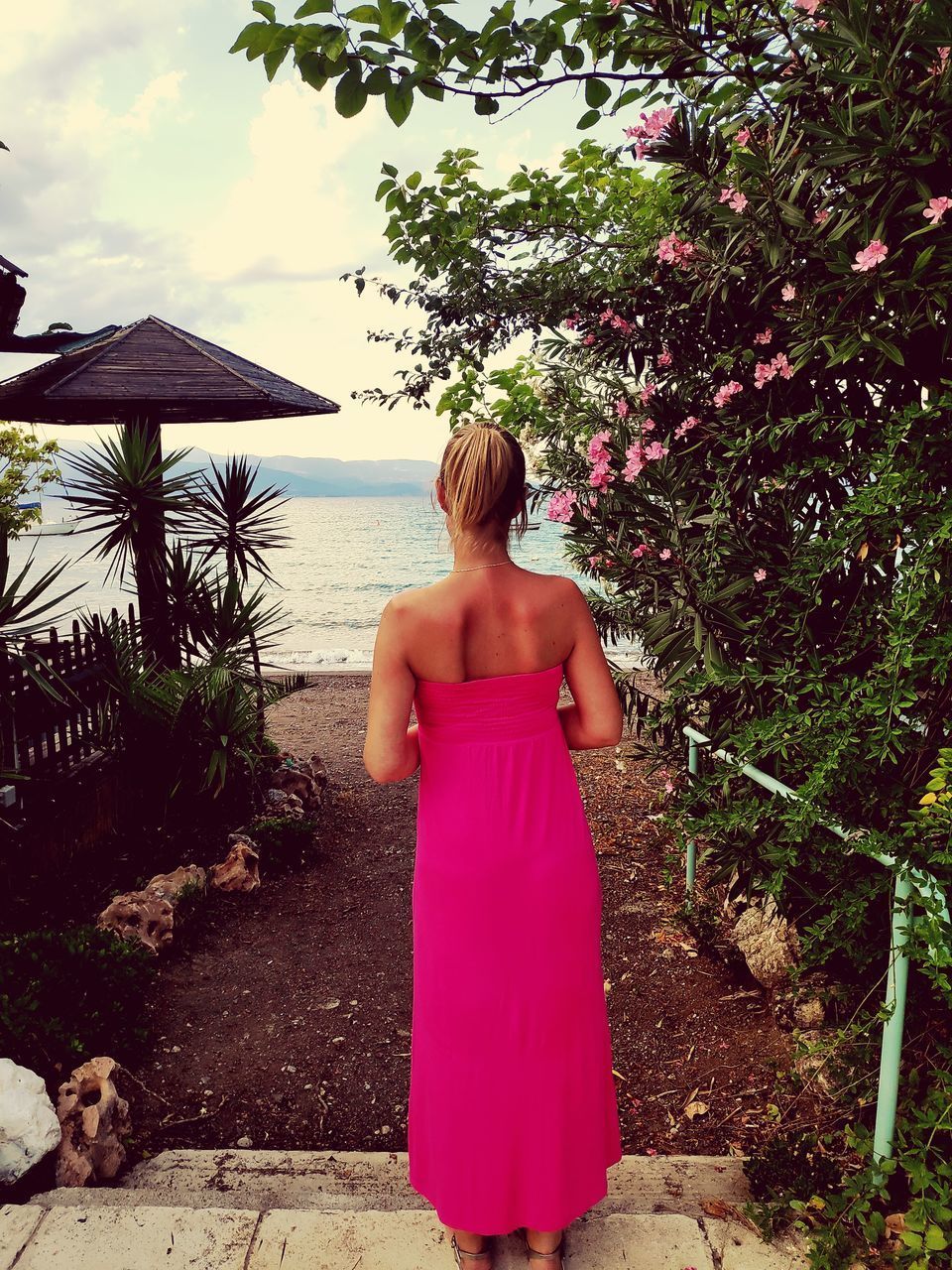 REAR VIEW OF WOMAN STANDING AGAINST PLANTS