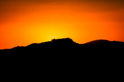 Scenic view of silhouette mountains against orange sky