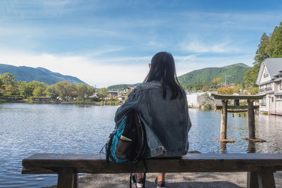 Rear view of woman sitting by lake against sky