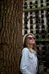 Young woman in sunglasses standing by tree