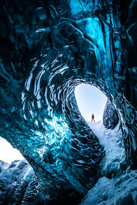Remote view of unrecognizable traveler standing in ice cave in winter during vacation in iceland