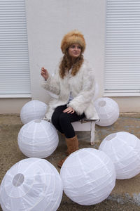 Woman in warm clothing smoking while sitting on bench amidst paper lanterns