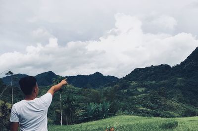 Rear view of man pointing at mountain against sky