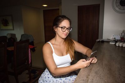 Young woman using mobile phone by table at home