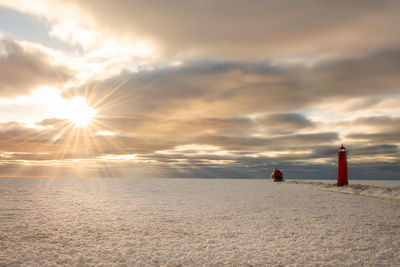 Lighthouse by frozen sea against sky during sunset