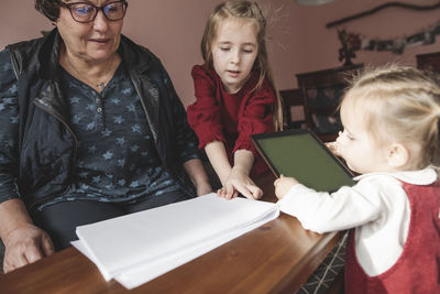 Two girls and grandmother playing with paper and tablet in living room