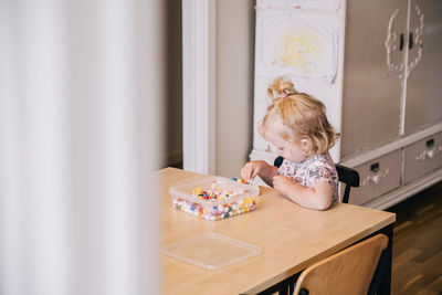 Blond girl playing with beads on table at home