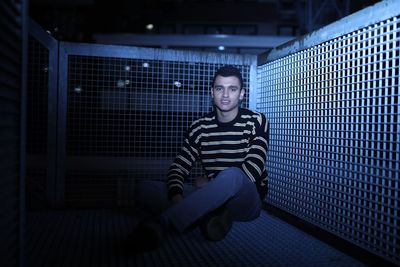 Portrait of young man sitting on metal at night