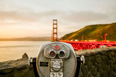 Close-up of coin-operated binoculars by sea against sky during sunrise