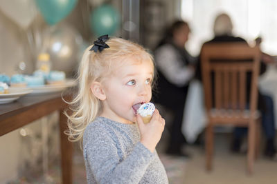 Cute girl eating cupcake at home during birthday party