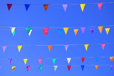 Low angle view of colorful buntings hanging against clear blue sky