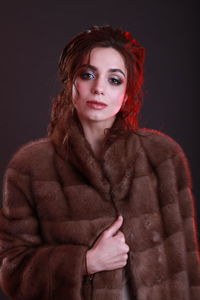 Portrait of beautiful young woman wearing fur coat against black background