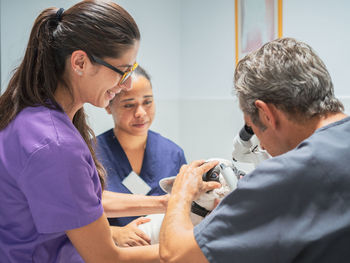 Cheerful women holding little dog for doctor during ear examination in veterinary clinic