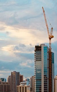 Low angle view of crane by buildings against sky