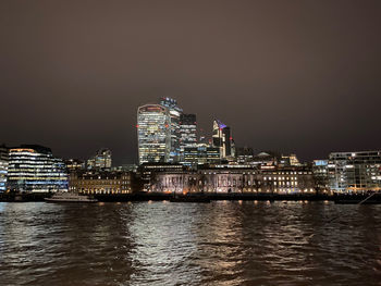 Illuminated buildings by thames river against sky at night in city of london