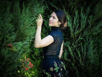 A young pretty woman in black clothes is standing near a bush