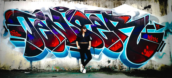 Full length of man standing against graffiti wall