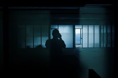 Silhouette woman sitting by window in dark room