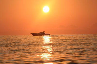 Silhouette boat in sea against orange sky